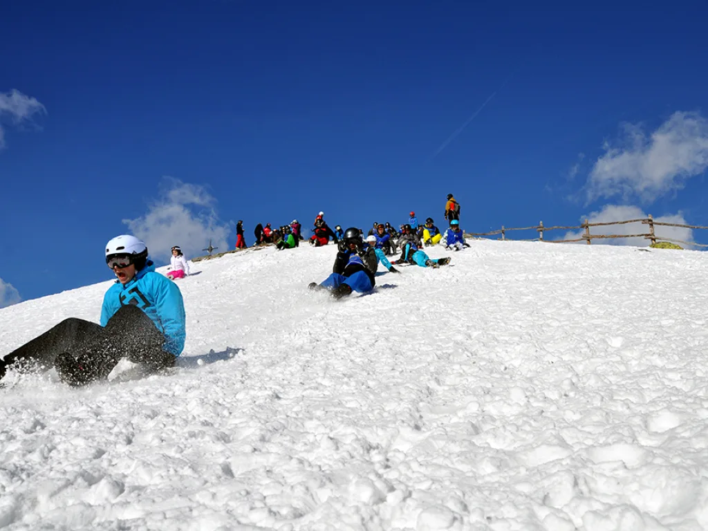 Jugendliche sitzen auf einer sonnigen Schneekuppe.